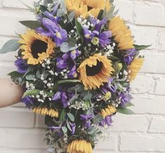 a bridal bouquet with sunflowers and baby's breath in front of a brick wall