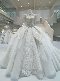 a white wedding dress on display in a room with stairs and chandelier above it