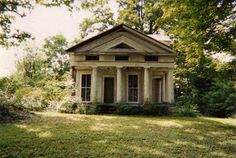 an old house sitting in the middle of a lush green field with trees around it