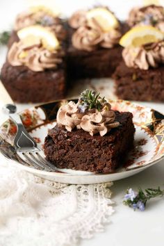 a piece of chocolate cake on a plate with a fork next to it and some lemon slices