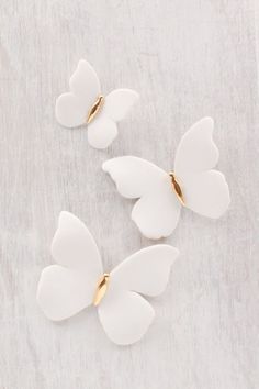 three white butterflies with gold accents on a gray background, one is shaped like a butterfly and the other is shaped like a flower