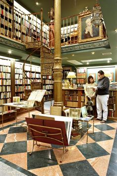 a man and woman looking at books in a library with a clock on the wall