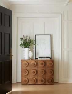 a wooden cabinet with vases and plants on it in front of a white wall