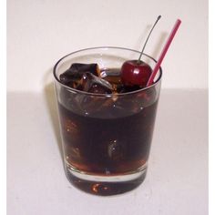 a glass filled with ice and cherries on top of a white table next to a red straw