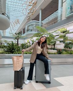 a woman sitting on top of a luggage bag next to a brown bag and a black suitcase