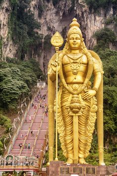 a large golden statue in the middle of a mountain with stairs leading up to it