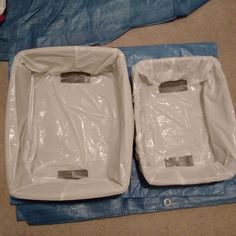 two empty white plastic bags sitting on top of a blue sheet covered floor next to each other