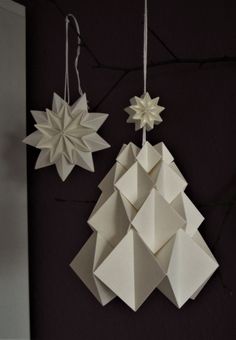 two white origami ornaments hanging on a black wall