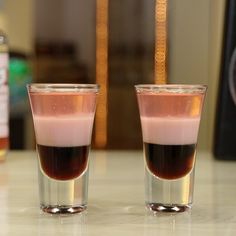 two shot glasses filled with liquid sitting on a table next to a bottle of alcohol