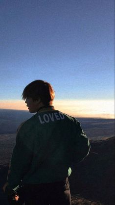 a man standing on top of a mountain with his back to the camera looking at the sky