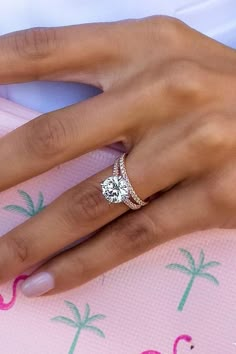 a woman's hand with a diamond ring on her finger and palm trees in the background