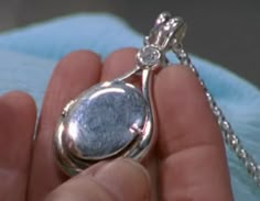 a person is holding a silver pendant in their hand with a chain attached to it