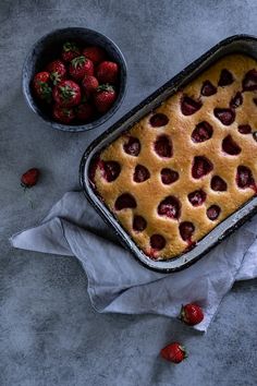 a strawberry cobbler and bowl of strawberries on a gray tablecloth next to it