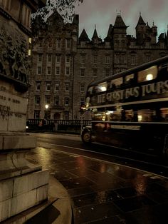 a double decker bus is driving down the street in front of an old building at night