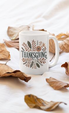 a white coffee mug with the words thanksgiving on it surrounded by leaves and fallen leaves