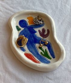 a ceramic dish with a person holding a ring in it's hand on a white table cloth