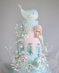 a three tiered cake with an octopus and mermaid theme on the top is decorated in pastel blue icing