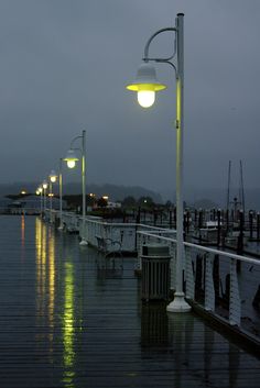 an empty pier at night with street lights and lanterns on the water's edge