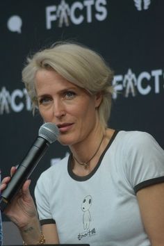 a woman talking into a microphone in front of a black wall with words on it