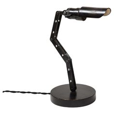 a desk lamp that is on top of a black stand with a cord attached to it