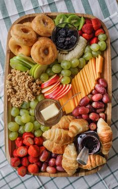 a wooden tray filled with different types of fruit and pastries on top of a checkered table cloth