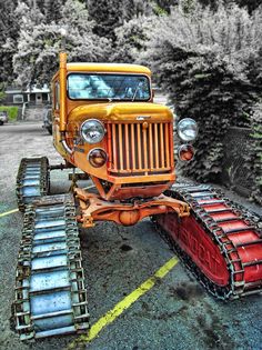 an old yellow truck is parked in a parking lot next to some snowplows