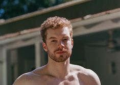 a shirtless man with no shirt standing in front of a building and looking at the camera