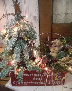 a small christmas tree in a red box with lights on it's sides and a teddy bear sitting next to it