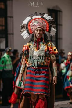 a native american man walking down the street in front of other people wearing headdress