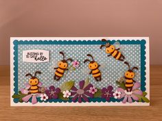 a card with three bees on it and flowers in the middle, sitting on a table