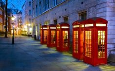 a row of red telephone booths sitting on the side of a street