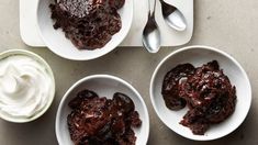 three white bowls filled with pudding and whipped cream on top of a table next to two spoons