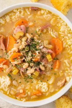 a white bowl filled with meat and rice soup next to some bread on the side