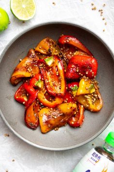 a bowl filled with sliced bell peppers and topped with sesame seeds next to a bottle of water