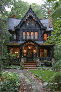 a large black house with lots of windows and stairs leading to the front door is surrounded by greenery