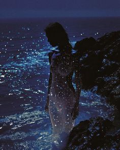 a woman standing in the ocean at night with her back to the camera and water splashing on her body