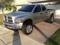 a silver truck parked in front of a house next to a driveway and palm tree