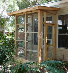 a chicken coop built into the side of a house in front of trees and bushes