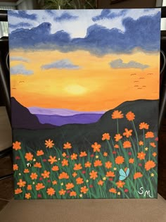 an easel painted with flowers in the foreground and a sunset in the background