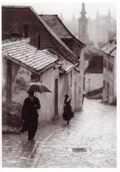 an old photo of people walking down the street in the rain with umbrellas over their heads