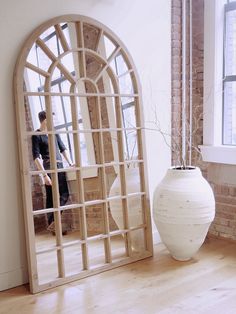 a large white vase sitting on top of a hard wood floor next to a window