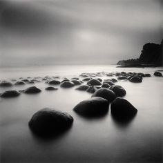 black and white photograph of rocks in the water at beach with dark sky behind them