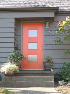 a red door sits in front of a gray house with potted plants on the steps