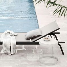 an outdoor lounge chair next to a swimming pool with pillows and blankets on the back