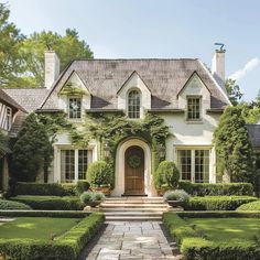 a large white house with lots of hedges and bushes around it's front door