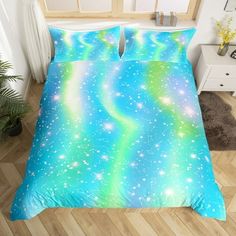 a bed covered in a blue and green comforter next to a plant on a wooden floor