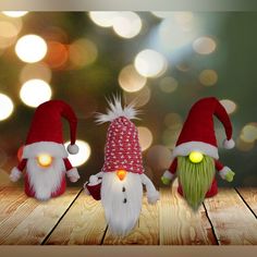 three christmas gnomes are sitting on a wooden table with bright lights in the background