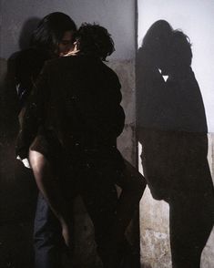 two people standing next to each other in front of a wall with their shadows on it