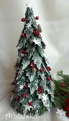 a small christmas tree with red berries, pine cones and snowflakes on it