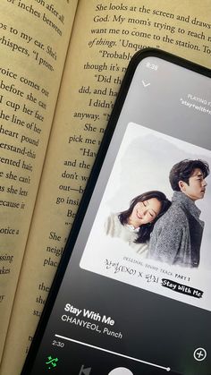 an open book next to a cell phone with the image of a man and woman on it